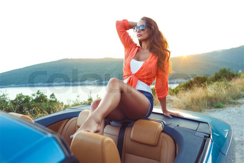 Beautiful woman sitting in cabriolet, enjoying trip on luxury modern car with open roof, fashionable lifestyle concept, stock photo