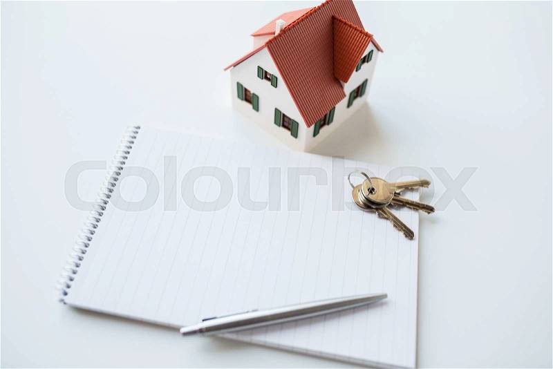 building, mortgage, real estate and property concept - close up of home model, house keys and notebook with pen, stock photo