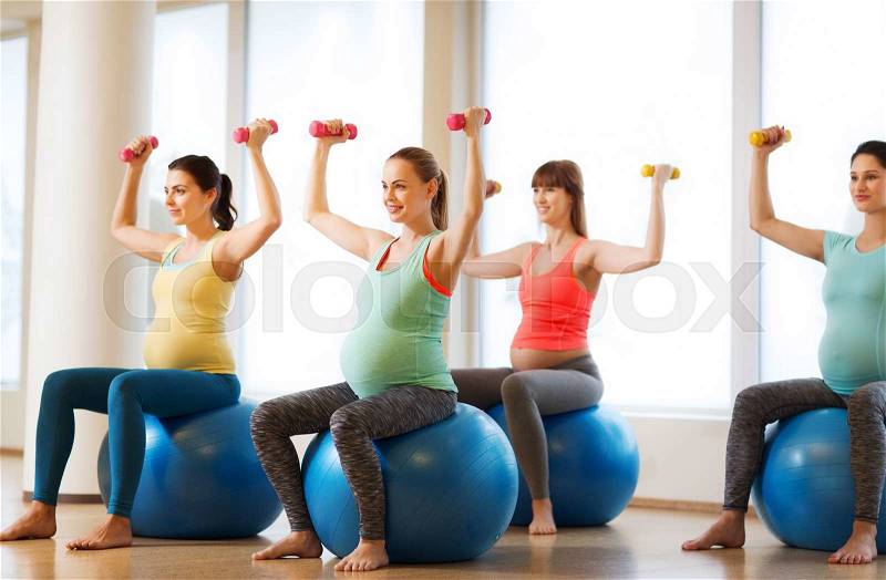 Pregnancy, sport, fitness, people and healthy lifestyle concept - group of happy pregnant women with dumbbells exercising on ball in gym, stock photo