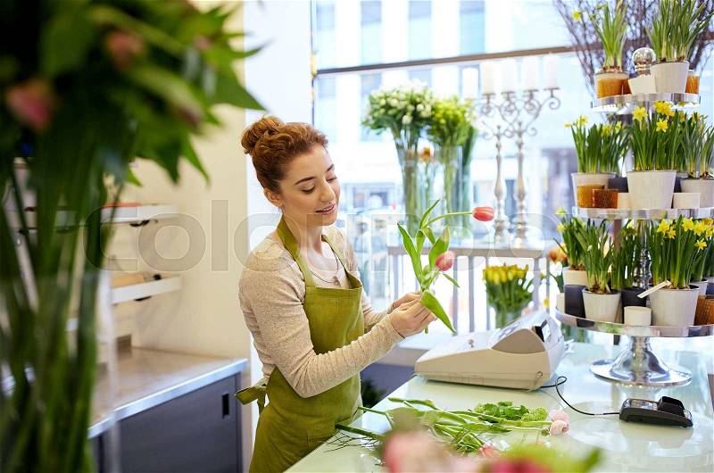People, business, sale and floristry concept - happy smiling florist woman making tulip bunch at flower shop, stock photo