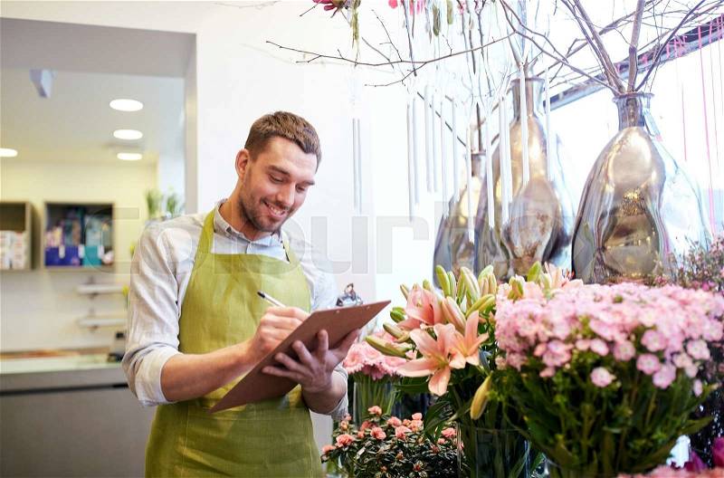 People, sale, retail, business and floristry concept - happy smiling florist man with clipboard writing and making notes order at flower shop, stock photo