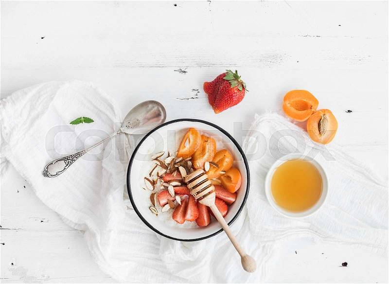 Healthy breakfast set. Rice cereal or porridge with fresh strawberry, apricots, almond and honey over white rustic wood backdrop, top view, copy space, stock photo