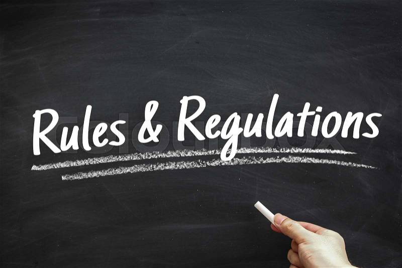 Text Rules And Regulations written on the blackboard with hand holding white chalk aside, stock photo