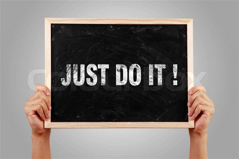 Hands holding small blackboard with text Just Do It against gray background, stock photo