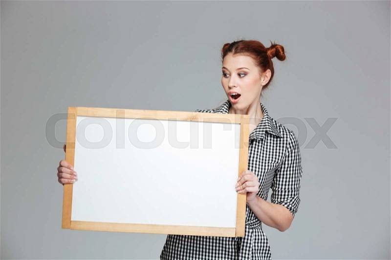 Amamzed cute young woman holding and looking at blank whiteboard , stock photo