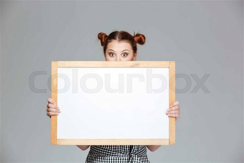 Funny lovely young woman hiding behind blank whiteboard , stock photo