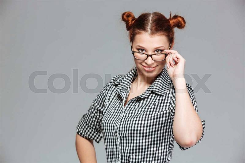 Smiling playful young woman looking over glasses over grey background , stock photo