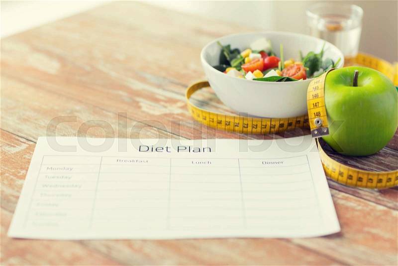 Healthy eating, dieting, slimming and weigh loss concept - close up of diet plan paper green apple, measuring tape and salad, stock photo
