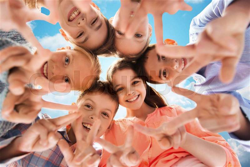 Childhood, fashion, friendship and people concept - happy smiling children showing peace hand sign and standing in circle over blue sky and clouds background, stock photo