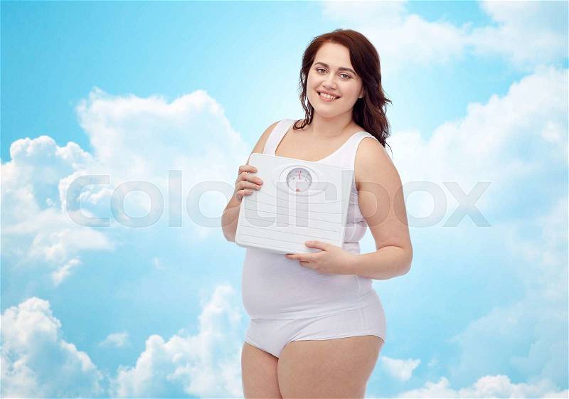 Weight loss, diet, slimming, plus size and people concept - happy young plus size woman in underwear holding scales over blue sky and clouds background, stock photo