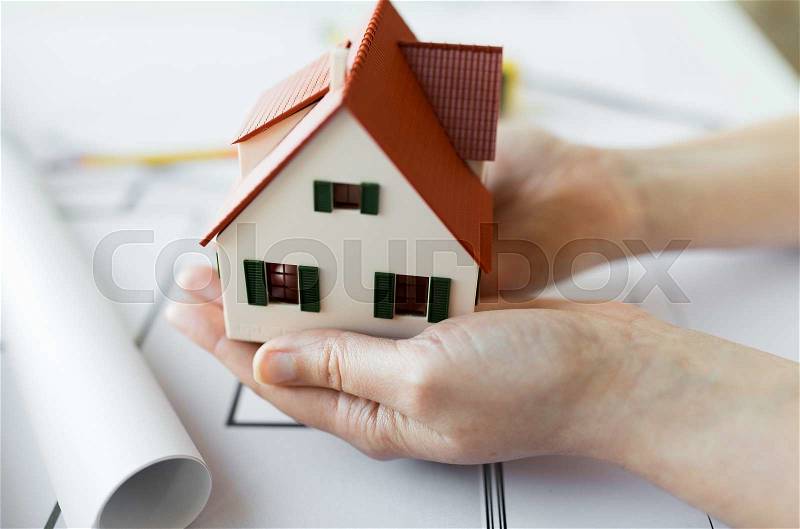 Architecture, building, construction, real estate and people concept - close up of architect hands holding living house model above blueprint on table, stock photo