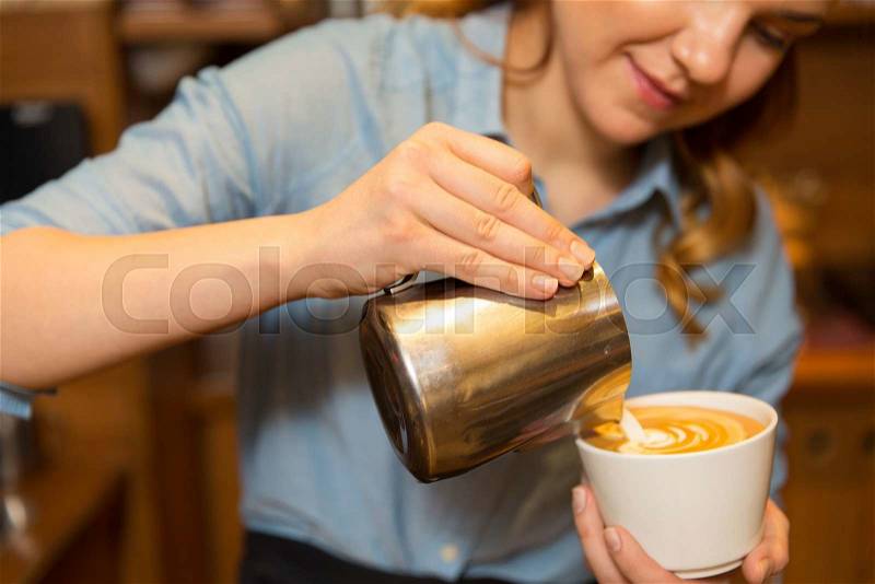Equipment, coffee shop, people and technology concept - close up of woman pouring cream to cup of coffee at cafe bar or restaurant kitchen, stock photo