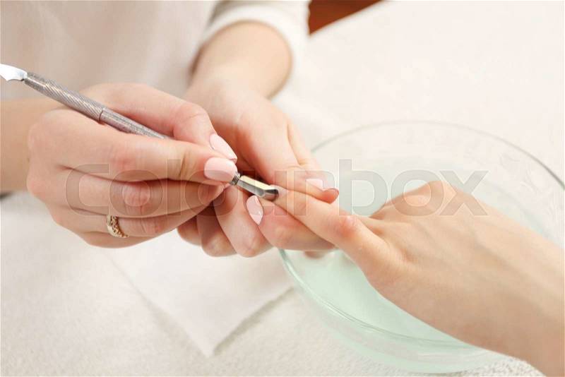 Closeup finger nail care by manicure specialist in beauty salon. Manicurist clear cuticle professional manicure tool, stock photo