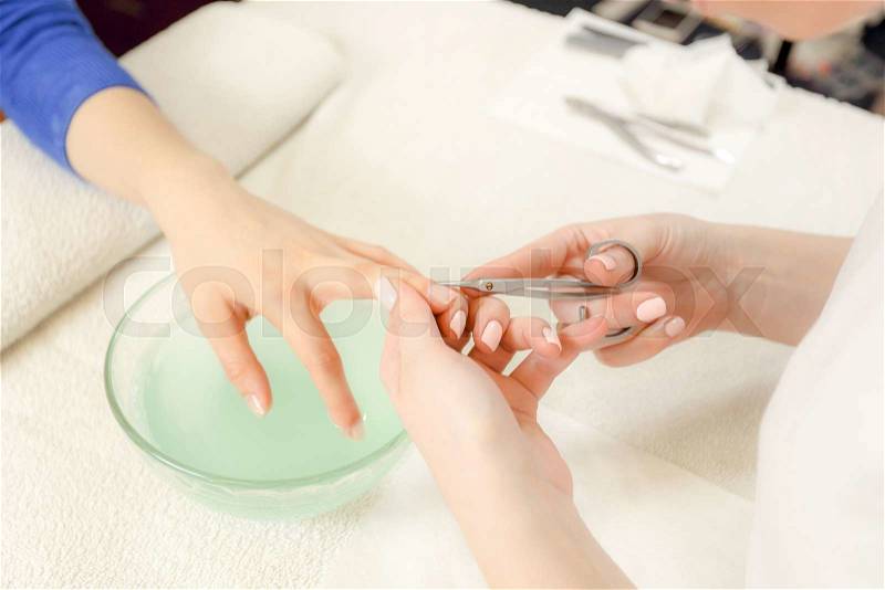 Closeup shot of a woman in a nail salon receiving a manicure by a beautician with nail scissors. Woman getting nail manicure. Beautician file nails to a customer, stock photo
