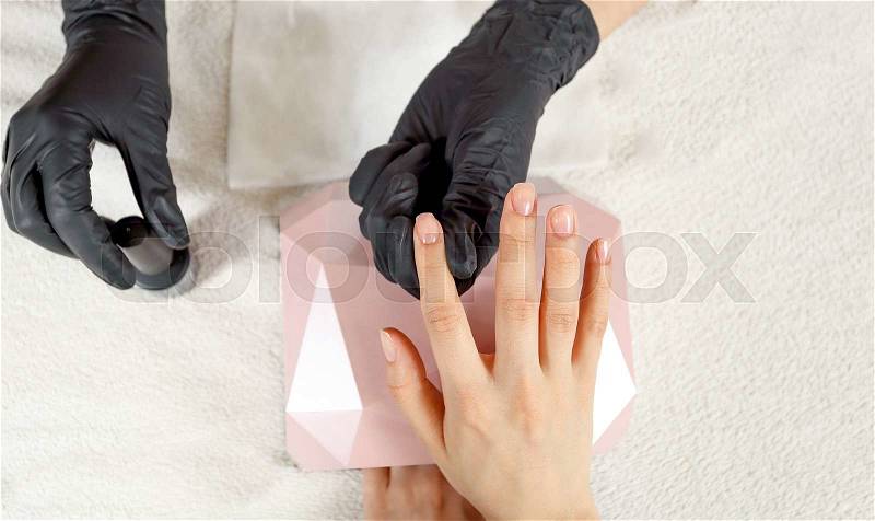 Top view manicurist holds customer hands. Fingernails are covered with clear nail polish, stock photo