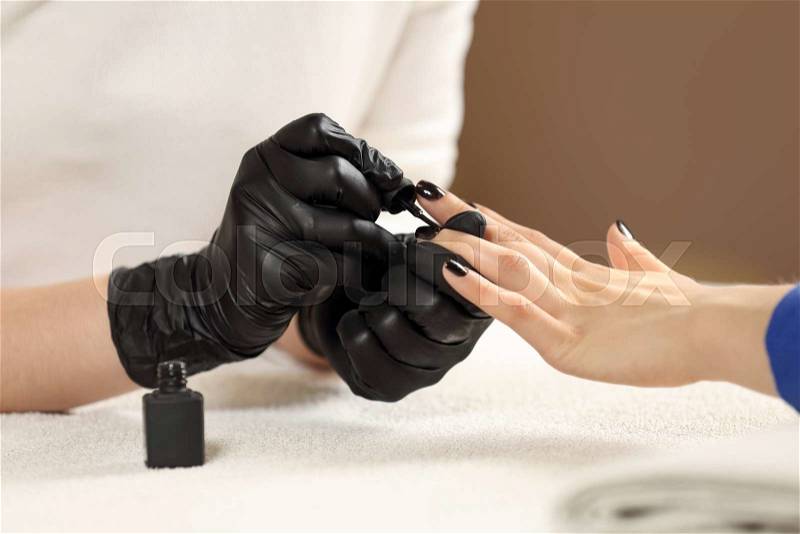 Closeup picture manicurist paints client nails in spa beauty salon. Manicure master in black gloves does manicure, stock photo