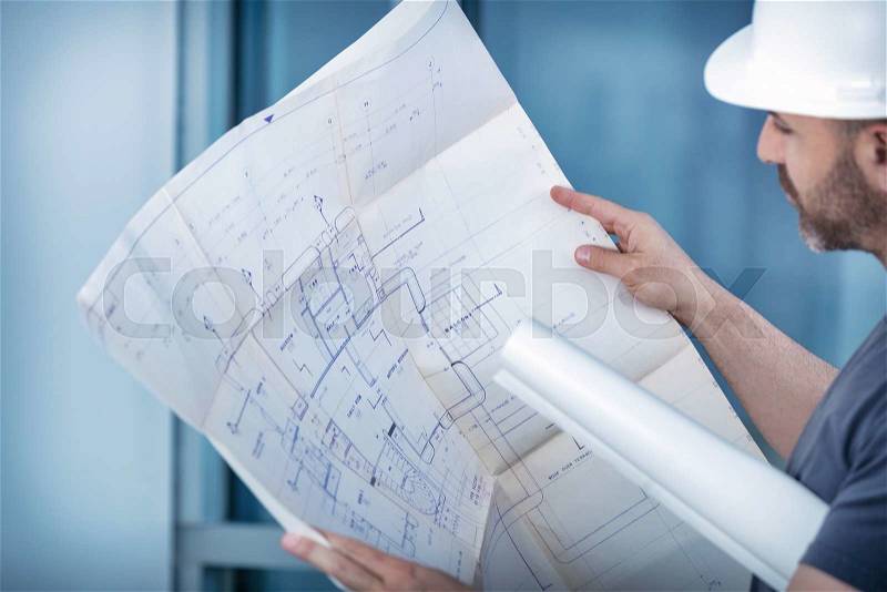 Portrait of an architect builder studying layout plan of the rooms, serious civil engineer working with documents on construction site, building and home renovation, professional foreman at work , stock photo