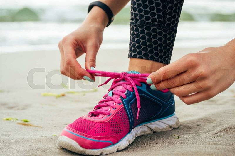 Female hands with manicure tie laces on pink and blue sneakers on the beach close up, stock photo