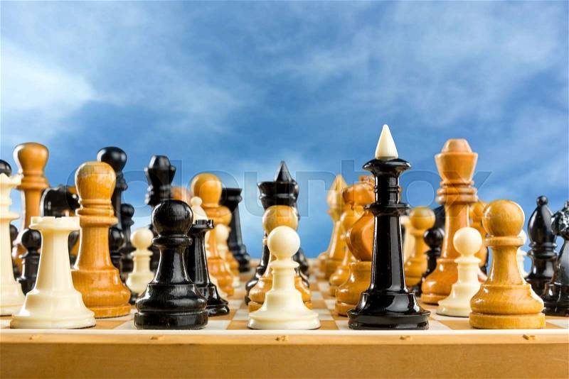 Many chess figures standing on the board over the sky, stock photo