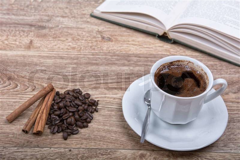 A cup of coffee and cinnamon with a book on a wooden background, stock photo