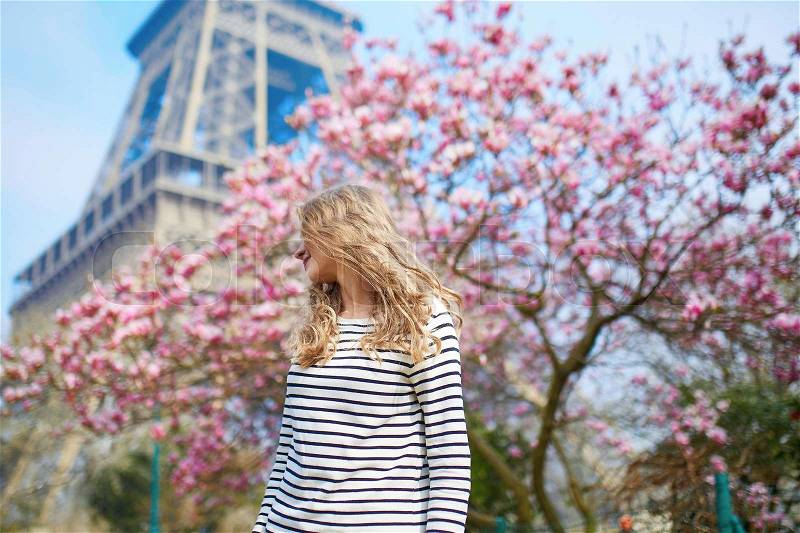 Cheerful young girl in Paris near the Eiffel tower and pink magnolia in full bloom, stock photo