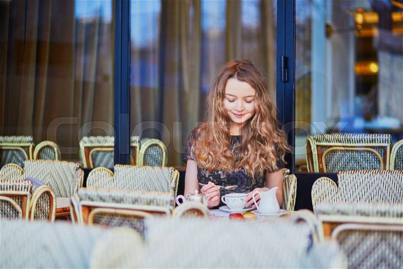 Beautiful Parisian woman in cafe, drinking coffee and eating macaroons, traditional French dessert, stock photo