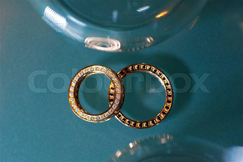 Two golden rings on turquoise glitter background, stock photo