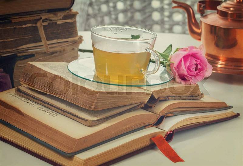 Cup of tea in glass with old books and rose flower, retro toned, stock photo