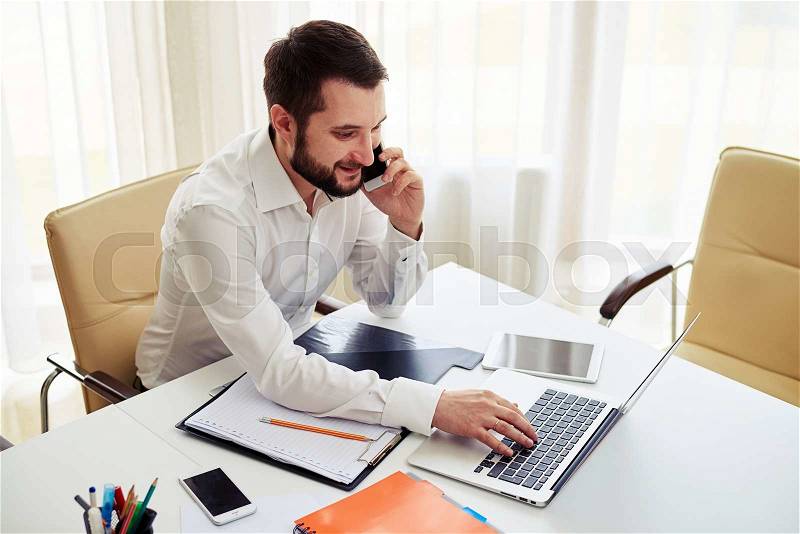 Man working on the laptop and calling someone on the phone in the modern white office, view from above, stock photo