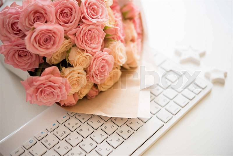 Bouquet of pink and beige roses on white computer keyboard, modern workplace closeup, stock photo