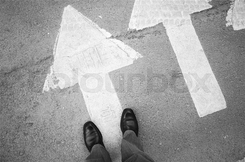 Male feet in new black shining leather shoes stand on asphalt pavement with white arrows pedestrian crossing road marking, first person view, stock photo