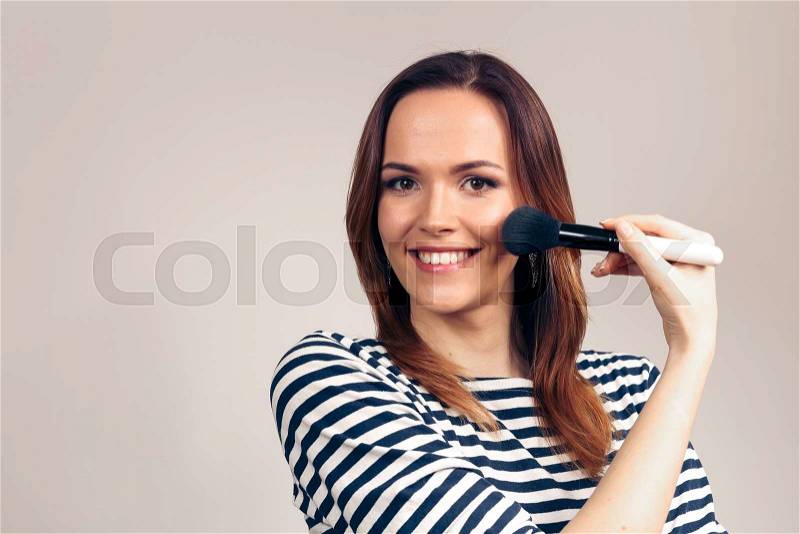 Closeup portrait of woman with makeup brush near face. Beauty woman applying makeup. Beautiful girl looking applying cosmetic with a big brush, stock photo