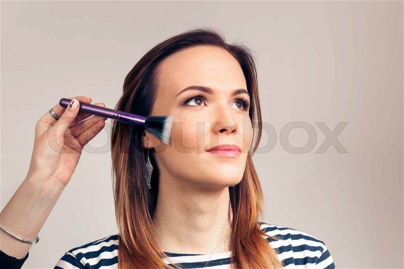 Makeup artist applying liquid tonal foundation on the face of the woman. Beauty Girl with Makeup Brush. Natural Make-up for Brunette. , stock photo