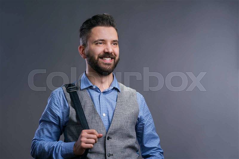 Hipster businessman in blue shirt and gray vest, studio shot on gray background, stock photo