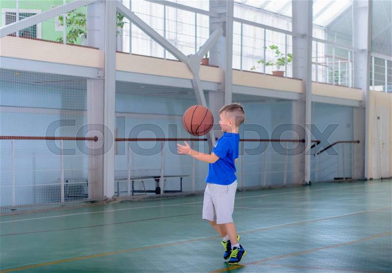 Young boy playing basketball on a bright indoor court with large windows preparing to catch the ball mid air, stock photo