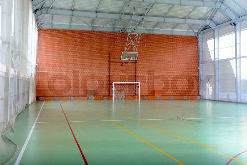 View across in indoor sports court with goalposts and a basketball hoop and net against a red brick wall, empty background view, stock photo