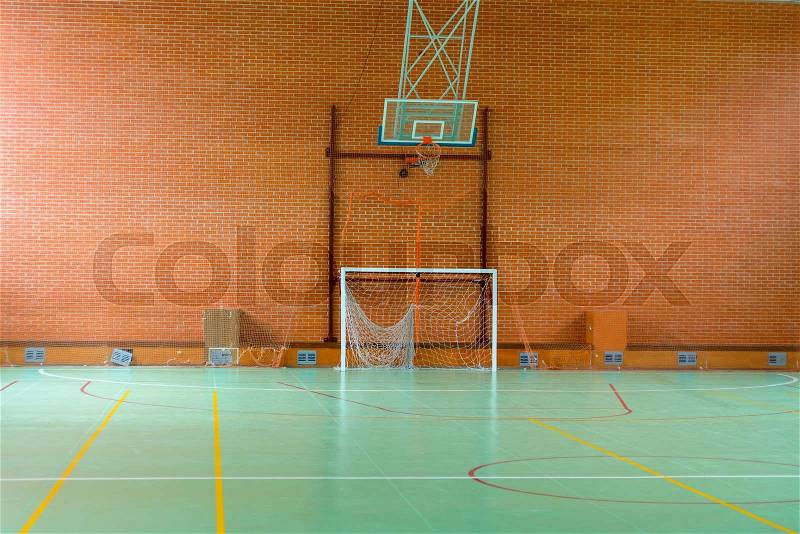 View across in indoor sports court with goalposts and a basketball hoop and net against a red brick wall, empty background view, stock photo