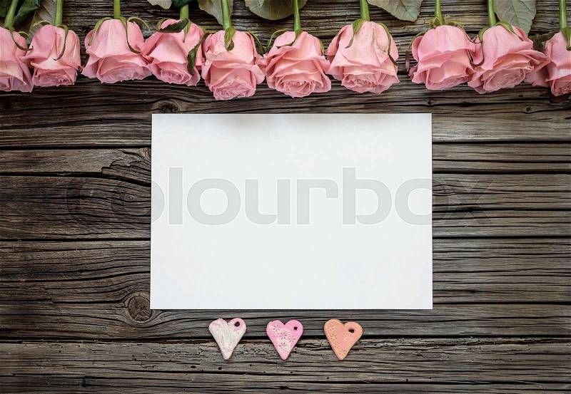 Single blank white horizontal paper with three paper heart shapes and row of pink roses in Valentines Day theme, stock photo