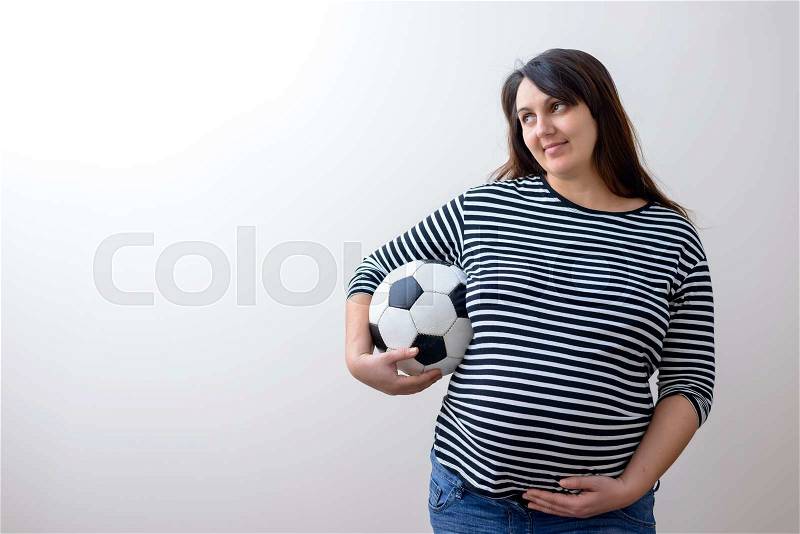 Grinning pregnant woman in striped shirt with football ball looking like a soccer mom, stock photo