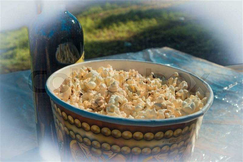 Camping. On the table, popcorn in a large glass and a bottle of wine. Against the background of blurred grass, stock photo