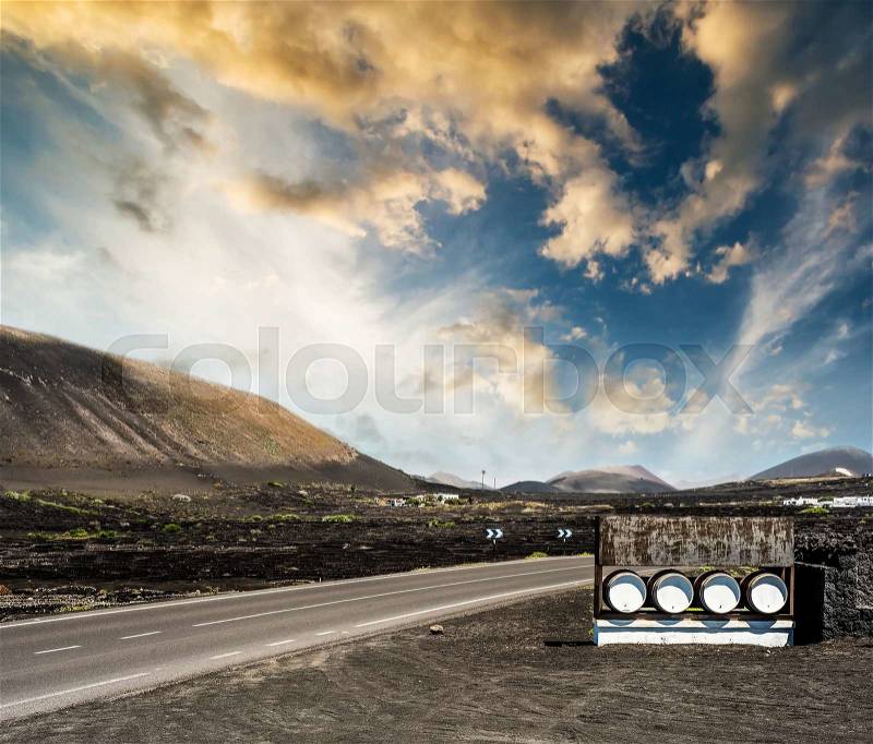 Road and restaurant advertisement casks near mountains against sunset sky in Lanzarote, Canary Islands, Spain, stock photo