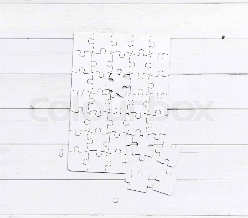 White unfinished puzzle isolated on white wooden table, stock photo