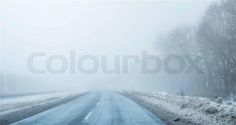 Foggy country road with dirty snow and trees on sides, stock photo