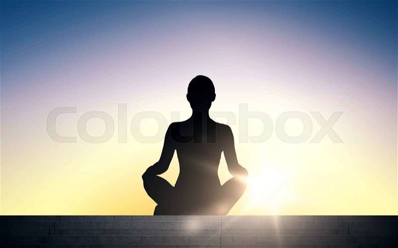 People, health, wellness and meditation concept - woman meditating in yoga lotus pose on stairs over sun light background, stock photo