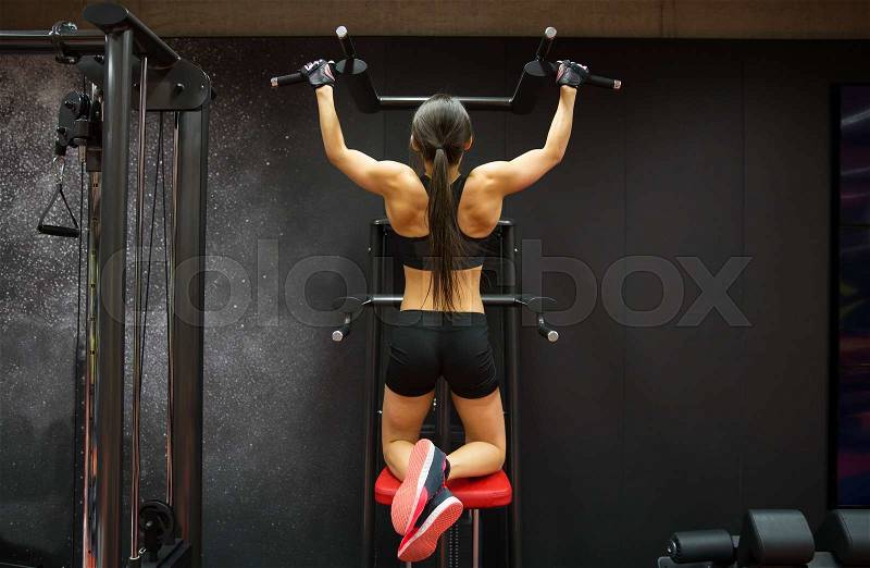 Sport, fitness, lifestyle and people concept - woman exercising and doing pull-ups in gym from back, stock photo