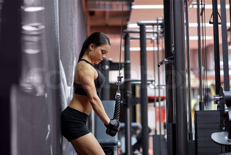 Sport, fitness, bodybuilding, lifestyle and people concept - woman flexing arm muscles on cable machine in gym, stock photo