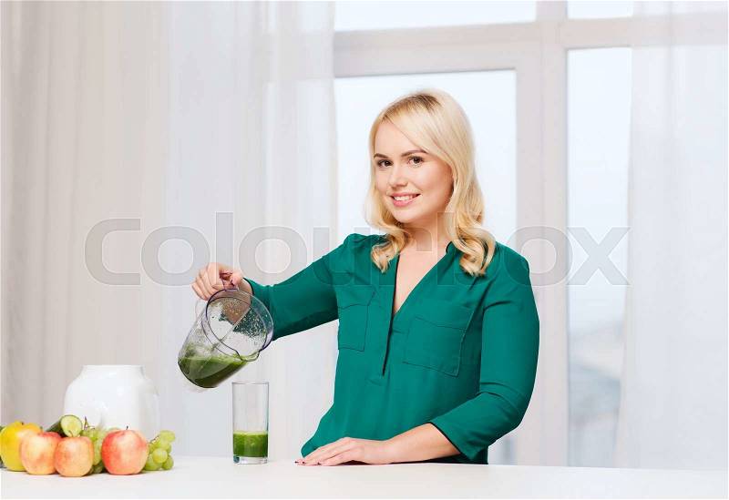 Healthy eating, cooking, vegetarian food, diet and people concept - smiling young woman with blender shaker jug pouring green vegetable smoothie or juice into glass at home kitchen, stock photo