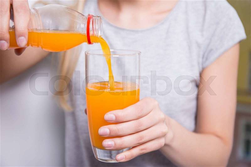 Close up of young woman pouring orange juice from the bottle to the glass, stock photo