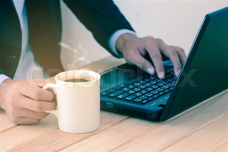 Businessman holding coffee cup and typing a laptop on wooden table. , stock photo