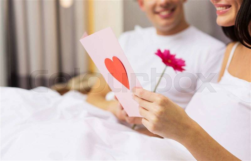 Love, relationships, holidays, valentines day and people concept - close up of happy couple in bed with postcard and flower, stock photo